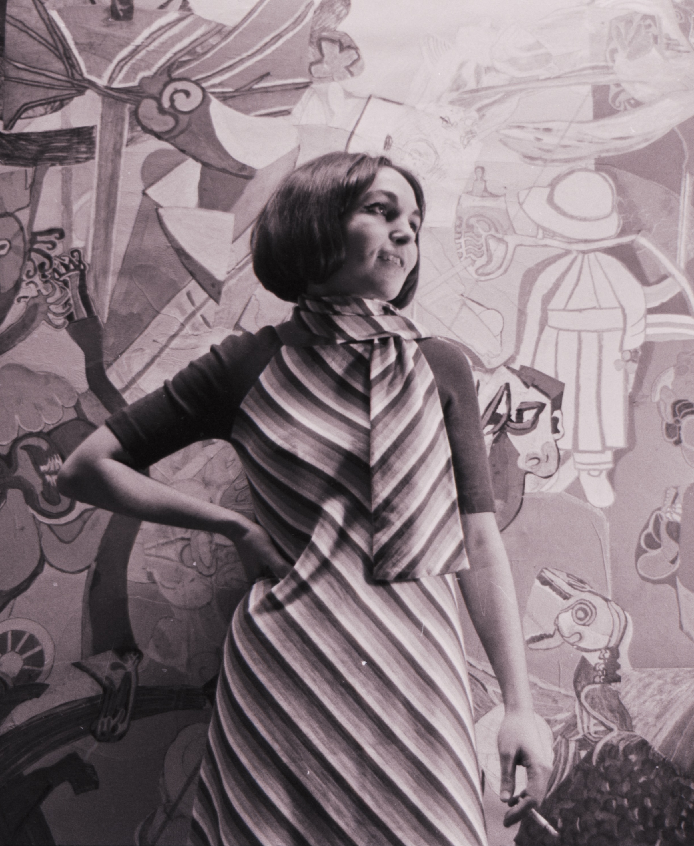 Bilde av en ung kvinne (Paula Rego) i sort hvitt. Hun har på seg en stripete kjole, og har plassert høyre hånd på hoften mens hun ser til siden.
