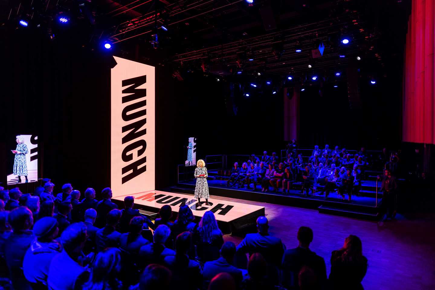 Dimmed blue lighting, the center stage with a woman presenting. 