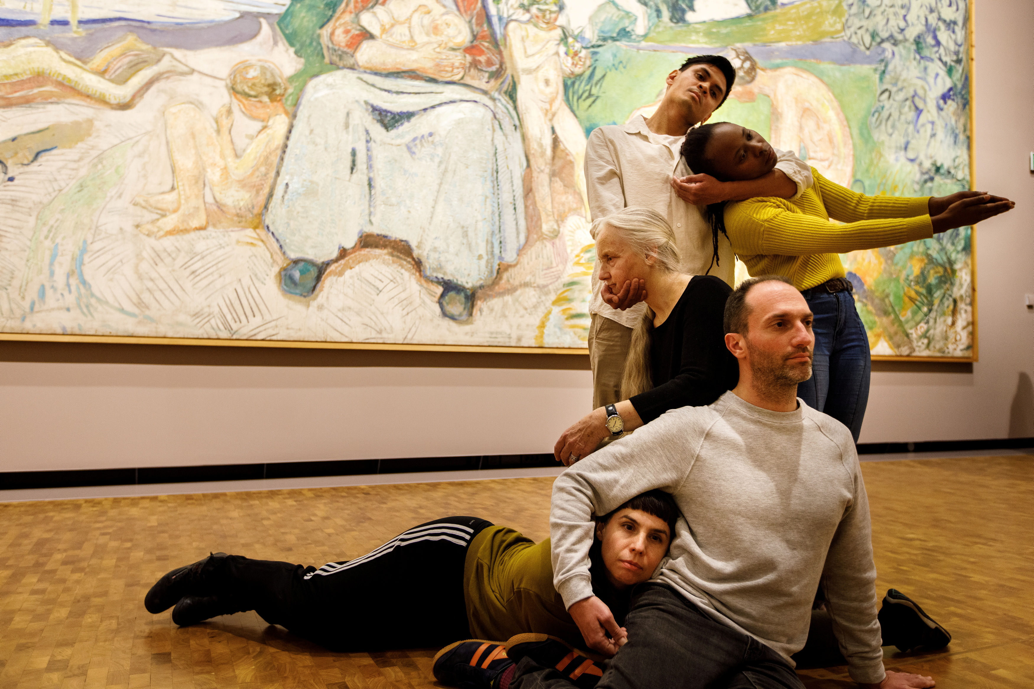 Five dancers in front of Edvard Munch's painting Alma Mater, performing Permanent Collection. They stand, sit, and lie intertwined with one another. Photograph.